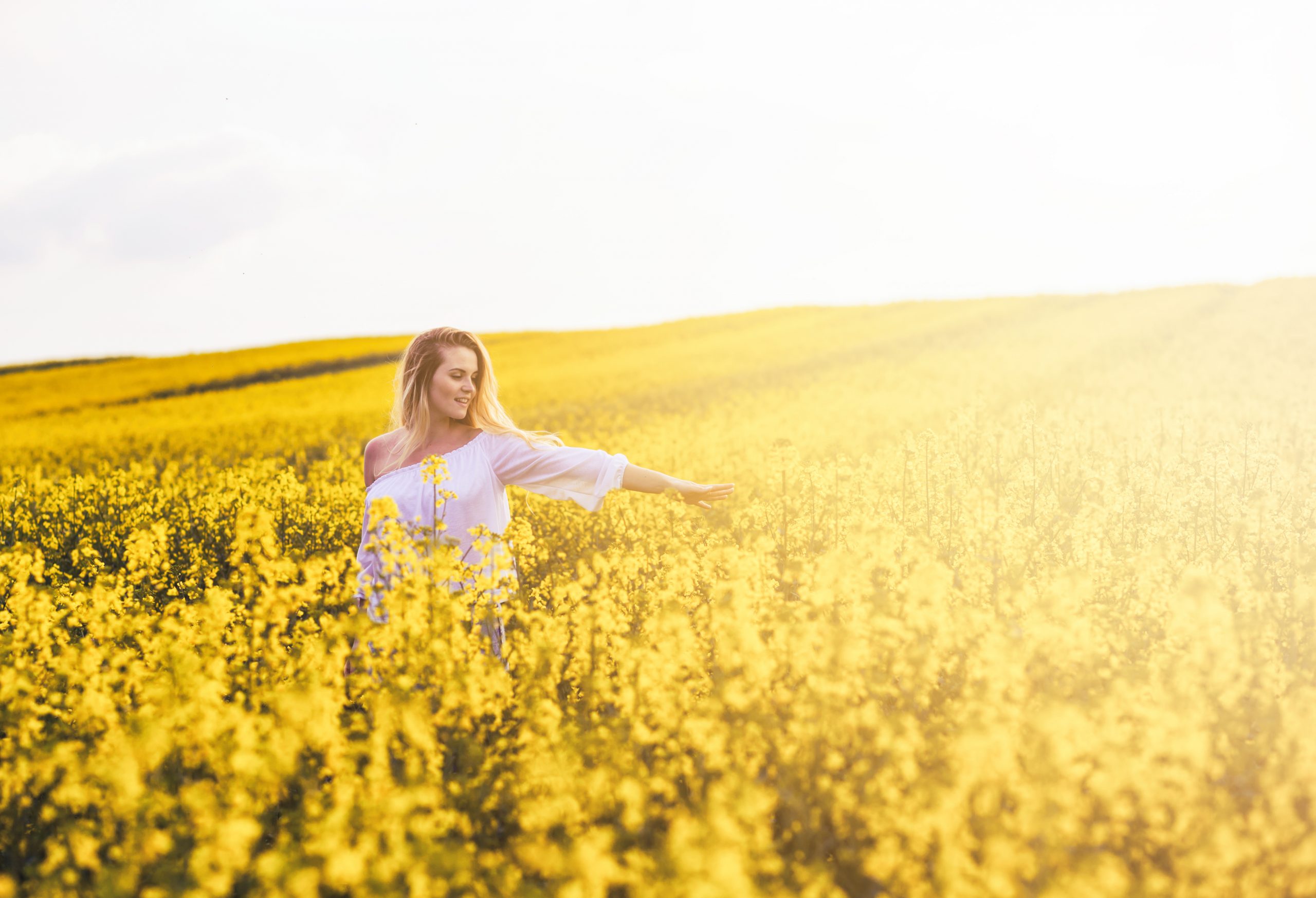 Smiling woman walking in yellow rapeseed field at sunset